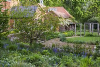 Un jardin contemporain aux couleurs du milieu de l’été est planté à l’est de la maison. Admirez un banc ombragé de jacinthes, de giroflées et de graminées.