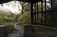Vue depuis une maison d'été en bois sur un chemin incurvé menant à travers un jardin boisé aux couleurs automnales. La maison du jardin, Yelverton. Automne, novembre