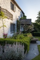 Ancienne maison en pierre galloise avec porche carrelé, rosa 'New Dawn' grimpant et plantation de style cottage avec un parterre de haie formel
