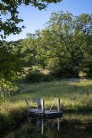 Grand étang faunique naturel, bordé de fleurs sauvages et de graminées, petit débarcadère avec sièges rustiques en bois