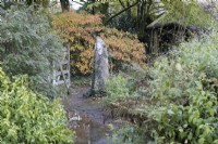 Un portail en bois ouvert avec un poteau en granit, traversé par un chemin et entouré d'arbres et d'arbustes au feuillage et aux couleurs d'automne. La maison du jardin, Yelverton. Automne, novembre
