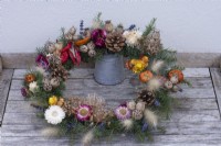 Une couronne de guirlande de jardinier, fabriquée à partir d'un cadre tissé recouvert de feuillage d'épinette et décorée de fleurs séchées, de cônes, de têtes de graines câblées et de fruits.