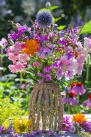 Bouquet d'été avec pois de senteur, roses, monarda, souci, échinops, persicaria et coquelicot dans un vase fait maison en pot de verre et corde en papier.