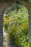 Vue à travers l'ouverture voûtée dans un mur de jardin en brique d'un parterre de fleurs avec Libertia, Meconopsis cambrica, Welsh Poppy, euphorbias et Anthriscus sylvestris, Cow Parsley. Peut.