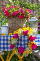 Impatiens dans un pot décoratif composé de corde en papier et de ficelle de chanvre et d'une couronne de fleurs d'été dont des glaïeuls, des tournesols et des carottes sauvages.
