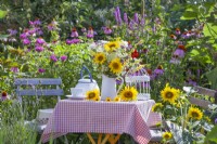 Table avec bouquet d'été de tournesols, verveine et fleurs sauvages dans une cruche en émail.