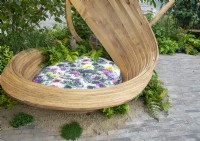 Un coin salon moderne et contemporain en bois courbé à la vapeur avec coussin floral à côté d'un patio pavé de briques d'argile avec des bords adoucis par des fougères - Dryopteris filix-mas