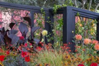 RHS COP26 Jardin caractéristique avec plantation de parterres de fleurs de divers dahlias, dont 'Bishop of Llandaff', Crocosmia 'Lucifer', graminées ornementales et Canna x generalis Cannova Bronze Scarlet - tonnelle en bois peinte en noir