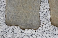 Détail de dalles de pierre irrégulières encastrées dans du gravier blanc.