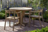 Table et chaises en bois sur un patio pavé de briques - écran métallique en acier, plantation de plantes vivaces mixtes 