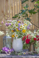 Composition florale d'été avec des fleurs sauvages, notamment des marguerites, des oeils de bœuf jaunes, des carottes sauvages, des campanules, des alliums et des roses rouges. 