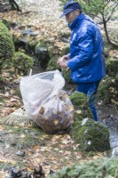 Jardinier portant des vêtements imperméables bleus, un chapeau et des gants nettoyant les feuilles du ruisseau 