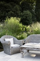 Meubles en osier autour d'une table en bois antique dans un jardin de campagne en juillet 