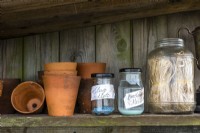 Pots en argile, bocaux avec granulés anti-limaces et mélange bordeaux et ficelles placés sur une étagère en bois 