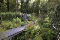 Jardin boisé avec passerelle au-dessus du ruisseau menant à la forêt d'aulnes noirs 