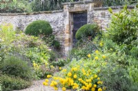 Les plantes vivaces se déversent sur un chemin de gravier qui mène à une porte encastrée dans un mur de pierre au Manoir, Little Compton. 