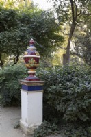 Une urne aux couleurs vives se dresse au sommet d’une colonne parmi une variété de feuillages. Parque de Maria Luisa, Séville, Espagne. Septembre 
