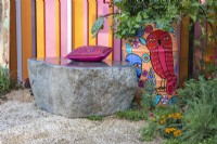 Un banc en pierre avec un coussin rose à côté d'un vieux tambour à huile peint planté de légumes, d'herbes et de fleurs. Le RHS et Eastern Eye Garden of Unity, concepteur : Manoj Malde. 