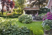 Cour avec salon de jardin et massifs plantés d'Hydrangea arborescens 'Annabelle', Hosta 'Frances Williams', Anémone et Hydrangea macrophylla. 