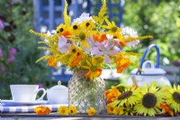 Bouquet de fleurs d'été avec Rudbeckia, Tropaeolum majus, Solidago et Malva dans un pot en verre décoré de ficelle. 