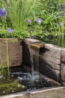 Traverses en bois récupéré transformées en jeu d'eau. La plantation comprend le géranium « Johnston Blue » - Caroline et Peter Clayton - Get Started Gardens - Nurturing Nature in the City, RHS Hampton Court Palace Garden Festival. 