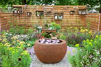 Petit jardin avec bol d'eau, table à plantes et étagères sur un mur en bois 