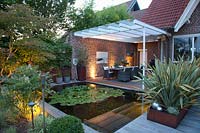 Terrasse éclairée avec du lin de Nouvelle-Zélande dans une jardinière en acier Corten, Phormium tenax Variegata 