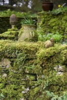 Mur de pierre moussu avec oiseau d'argile aux jardins de Cerney House en mars 