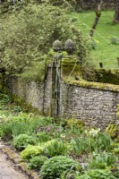 Mur en pierre avec entrée encadrée par des poteaux de porte surmontés d'embouts d'ananas aux jardins de Cerney House en mars 