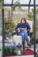 Femme lisant un magazine dans une grande serre décorée de guirlandes lumineuses et de plantes mélangées 