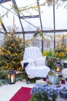 Chaises en plastique recyclé avec couvertures et coussins dans une serre décorée de plantes mélangées et de guirlandes lumineuses 