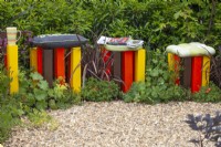 Poteaux jaunes, marron et rouges avec coussins pour s'asseoir dans un parterre de fleurs contenant du Phormium et de l'Alchemilla mollis dans le jardin 'In the Loop' du BBC Gardener's World Live 2015 