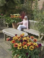 Femme assise dans un coin salon de jardin avec des pots plantés de tulipes 