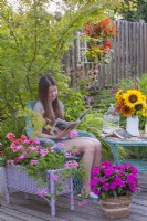 Une jeune femme aime lire un magazine sur une terrasse d'été ornée de pots plantés de pélargoniums et d'Impatiens. 