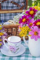 Tasse à thé et bouquet d'été contenant du Dahlia, du Tanacetum vulgare et de l'Astrantia dans un pichet blanc. 