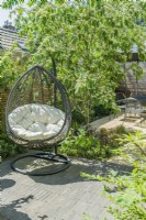 Une chaise de jardin extérieure suspendue dans un petit jardin urbain ensoleillé avec de l'ombre tachetée fournie par un cotonéaster à plusieurs tiges. Juin. 