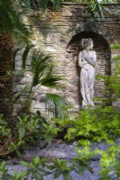 Vue sur le jardin semi-tropical « secret » avec fougères arborescentes, Acer palmatum et palmiers, statue classique installée dans un mur de pierre 