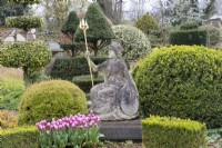 Statue de Britannia avec inscription latine et pots en terre cuite avec tulipes. Topiaire d'If et fort derrière. Avril. Printemps. 