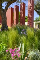 Vue sur le jardin méditerranéen avec des piliers de compartiment orange plantés de Stipa tenuissima et de grands arbres d'olivier. JuneDesigner - Alan Rudden 